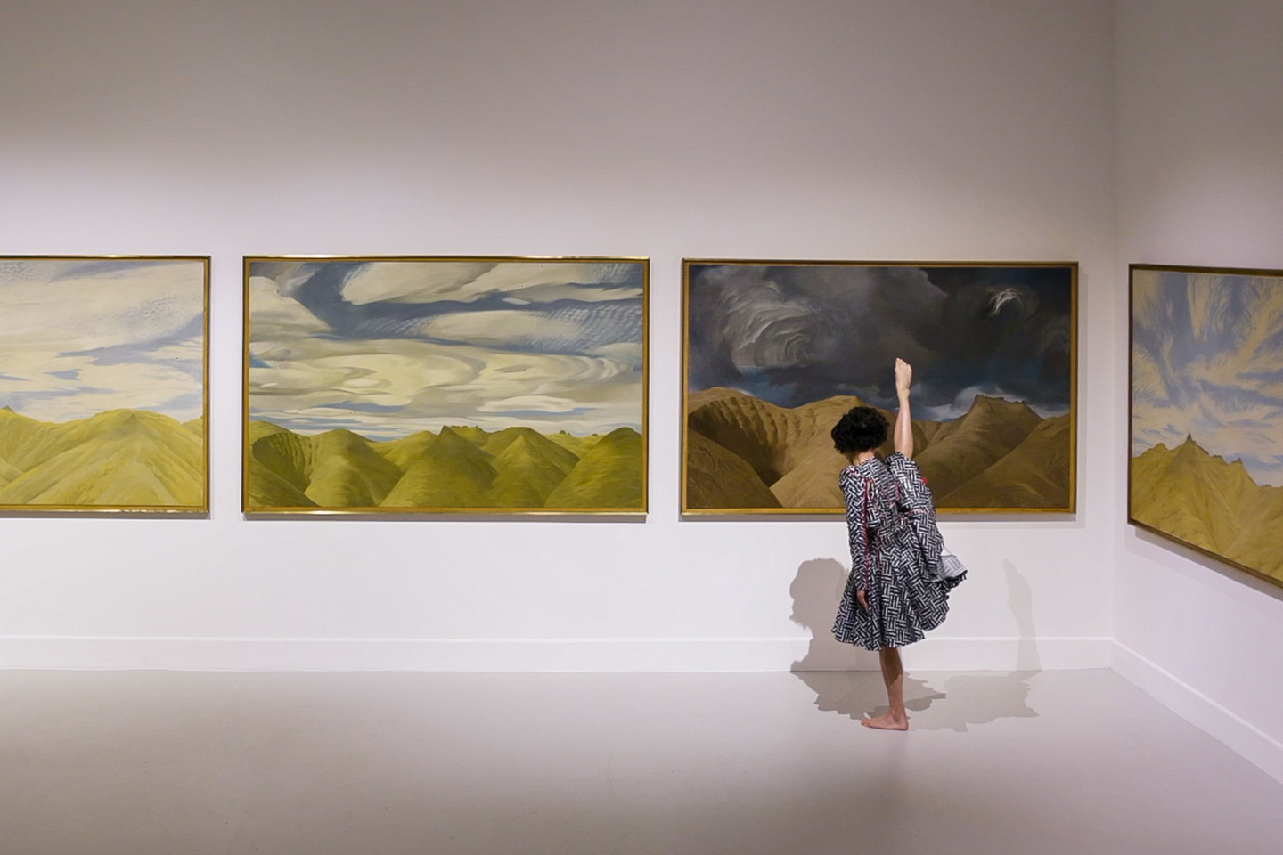 An elaborately costumed dancer stands on one leg in front of a landscape painting by W. A. Sutton. An elaborately costumed dancer stands on one leg in front of a landscape painting by W. A. Sutton.